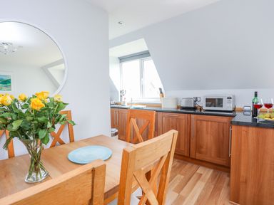 A kitchen with wooden cabinets and table with yellow flowers on it at Isallt Cove in Trearddur Bay
