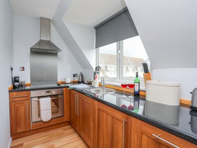 A kitchen with wooden cabinets a black countertop a window and various kitchen appliances at Isallt Cove in Trearddur Bay