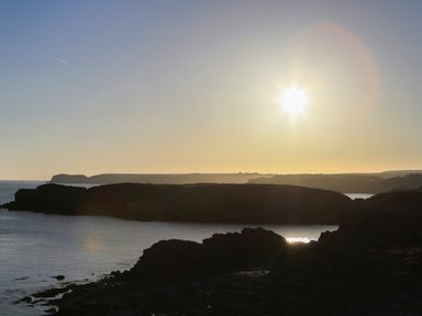 A rocky coastline with the sun low in the sky over the sea at Isallt Cove in Trearddur Bay