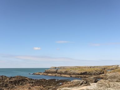 A rocky coastline with patches of grass and the sea under a blue sky at Isallt Cove in Trearddur Bay