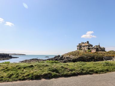 A coastal scene with a large stone house on rocky terrain beside the sea at Isallt Cove in Trearddur Bay