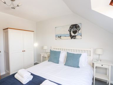 A bedroom with a double bed two blue pillows two bedside tables with lamps a white wardrobe and a painting of a dog at Isallt Cove in Trearddur Bay