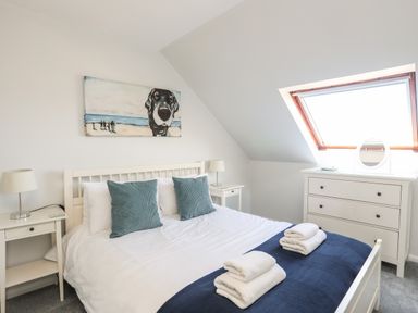 A bedroom with a bed two bedside tables with lamps a chest of drawers and a skylight window at Isallt Cove in Trearddur Bay