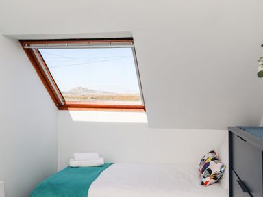 A small bedroom with a single bed near a slanted window showing an outdoor landscape at Isallt Cove in Trearddur Bay