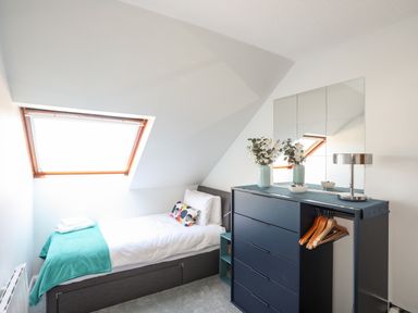 A small bedroom with a single bed under a skylight window and a chest of drawers with hangers on the side at Isallt Cove in Trearddur Bay