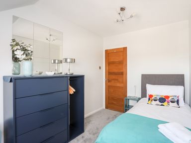 A bedroom with a blue dresser with hangers a bed with colorful pillow a small side table and a wooden door at Isallt Cove in Trearddur Bay