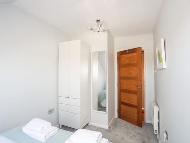 A bedroom with white wardrobe a mirror wooden door and towels on bed at Isallt Cove in Trearddur Bay