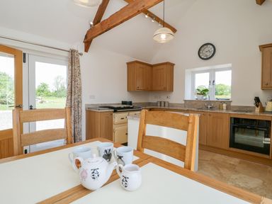 A kitchen with wooden cabinets a dining table with teapot and cups and a clock on the wall at Golden Valley Barn in Oldbury-On-Severn