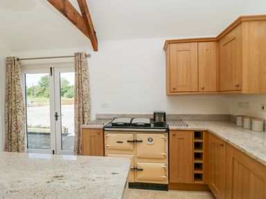 A kitchen with wooden cabinets cream oven granite countertops and floral curtains at Golden Valley Barn in Oldbury-On-Severn