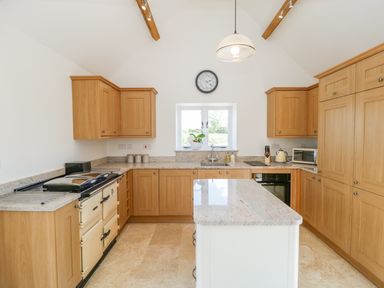 A kitchen with wooden cabinets, a kitchen island, a window with a plant, and a clock on the wall at Golden Valley Barn Oldbury-On-Severn