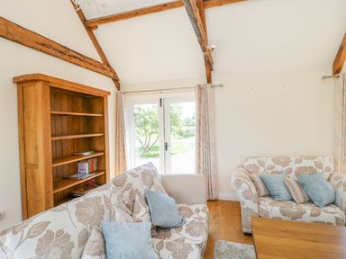 A sitting room with sofas a wooden bookshelf and glass doors leading outside at Golden Valley Barn in Oldbury-On-Severn