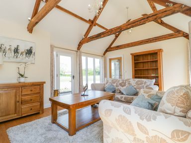 A living room with floral sofas a wooden coffee table wooden beams and shelves at Golden Valley Barn in Oldbury-On-Severn