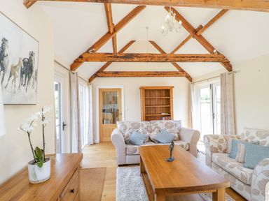 A living room with exposed wooden beams two sofas a wooden coffee table and a wooden bookshelf at Golden Valley Barn in Oldbury-On-Severn
