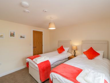 A bedroom with two single beds with orange throws and pillows a bedside table with a lamp and framed pictures on the wall at Golden Valley Barn in Oldbury-On-Severn
