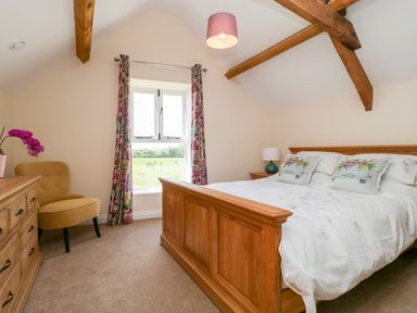 A bedroom with a wooden bed and dresser a yellow chair and floral curtains at Golden Valley Barn in Oldbury-On-Severn