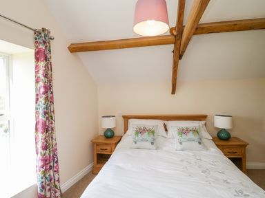 A bedroom with a double bed white bedding floral pillows two wooden bedside tables lamps and floral curtains at Golden Valley Barn in Oldbury-On-Severn