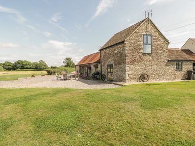 A stone house with a tiled roof and outdoor chairs and table on a gravel area surrounded by grass at Golden Valley Barn in Oldbury-On-Severn