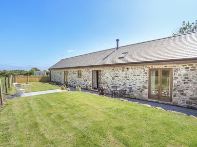 A stone exterior building with wooden doors and windows and chairs on the lawn at Y Bwthyn in Brynsiencyn