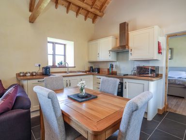 A kitchen with wooden dining table and four chairs white cabinets and a window at Y Bwthyn in Brynsiencyn