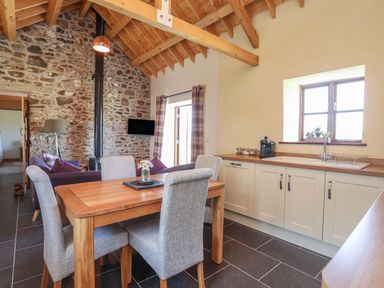A kitchen and dining area with wooden table and upholstered chairs and stone wall at Y Bwthyn in Brynsiencyn