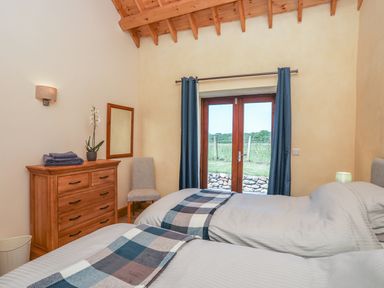 A bedroom with two single beds a wooden chest of drawers a chair and a window with blue curtains at Y Bwthyn in Brynsiencyn