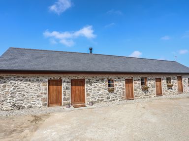 Exterior of a stone building with six wooden doors and two small windows with flower boxes at Y Bwthyn in Brynsiencyn