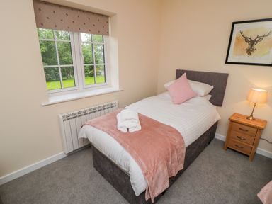 A bedroom with a single bed with pink and white bedding beside a window and wooden nightstand with a lamp at Ryedale Country Lodges - Hazel Lodge Kirkbymoorside