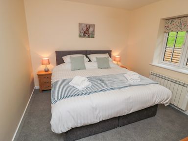 A bedroom with a double bed two bedside tables with lamps window with floral blind and a rabbit painting on the wall at Ryedale Country Lodges - Hazel Lodge in Kirkbymoorside