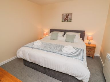 A bedroom with a double bed bedside tables lamps and a rabbit painting on the wall at Ryedale Country Lodges - Hazel Lodge in Kirkbymoorside