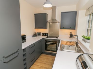 A kitchen with grey cabinets a stove oven a microwave a kettle a toaster and a sink at Ryedale Country Lodges - Hazel Lodge Kirkbymoorside