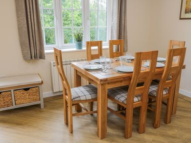 A dining room with a wooden table set for six and a bench with baskets under a window at Ryedale Country Lodges - Hazel Lodge in Kirkbymoorside