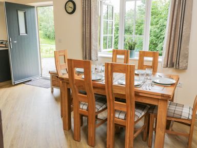 A dining area with a wooden table set with plates and cutlery six wooden chairs and an open door at Ryedale Country Lodges - Hazel Lodge in Kirkbymoorside