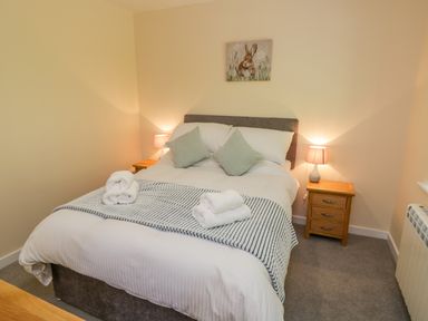 A bedroom with a bed with two pillows and folded towels two bedside tables with lamps and a rabbit painting on the wall at Ryedale Country Lodges - Willow Lodge in Kirkbymoorside