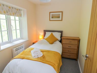 A bedroom with a single bed a yellow blanket a wooden chest of drawers and a window at Ryedale Country Lodges - Willow Lodge in Kirkbymoorside