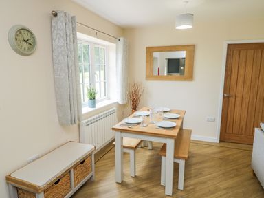 A dining area with a wooden table set for four and benches near a window and a wooden door at Ryedale Country Lodges - Willow Lodge in Kirkbymoorside