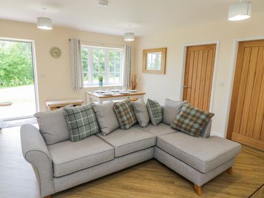 A living room with a grey corner sofa and dining table near a window at Ryedale Country Lodges - Willow Lodge Kirkbymoorside