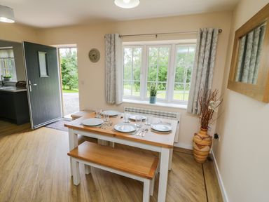 A dining area with a wooden table set for four near a window and an open door at Ryedale Country Lodges - Willow Lodge in Kirkbymoorside