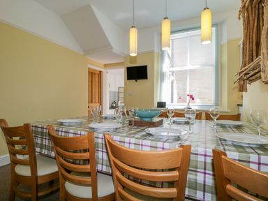 A dining room with a table set with plates and glasses and wooden chairs at Sefton House in Keswick