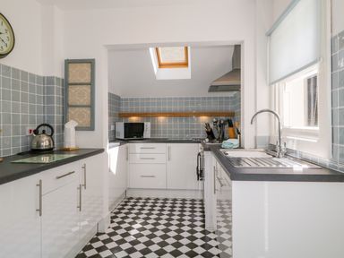 A kitchen with black and white checkered floor a window with blind a sink countertop microwave and a kettle at Sefton House in Keswick