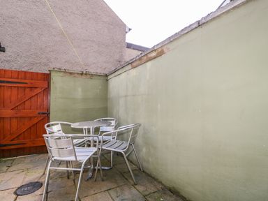 An outdoor patio area with a metal table and four metal chairs near a wooden gate at Sefton House in Keswick