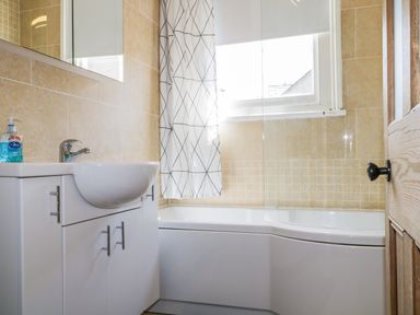 A bathroom with a white sink cabinet and a bathtub with a shower curtain at Sefton House in Keswick