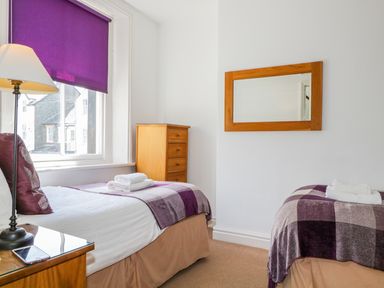 A bedroom with two single beds blankets and towels a chest of drawers and a window with a purple blind at Sefton House in Keswick
