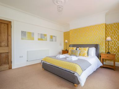 A bedroom with a bed with yellow and gray bedding bedside tables with lamps and geometric yellow wallpaper behind the bed at Sefton House in Keswick