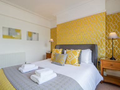 A bedroom with a bed featuring yellow and grey pillows and a patterned yellow wallpaper at Sefton House in Keswick