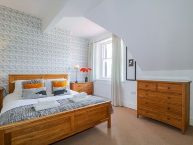 A bedroom with a wooden bed chest of drawers a window and a bedside table at Sefton House in Keswick