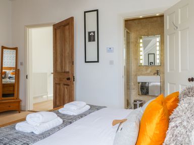 A bedroom with a bed with folded towels orange pillows and a gray blanket next to a wooden door and a bathroom at Sefton House in Keswick