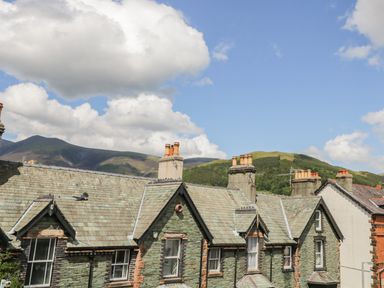 Roofs of stone buildings with chimneys with hills and clouds in the background at Sefton House in Keswick