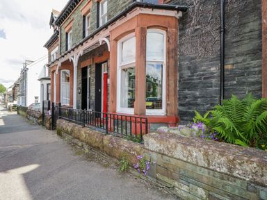 A stone house with red window frames and a red door with black iron railings at Sefton House in Keswick