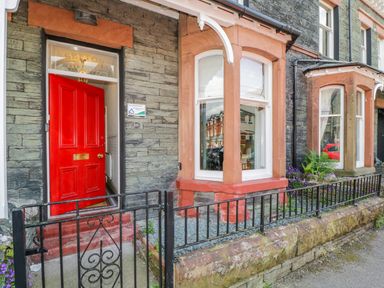 A stone house exterior with a red door black iron gate and bay windows at Sefton House in Keswick