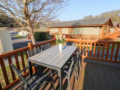An outdoor deck with a table and six chairs and a vase of flowers at Serendipity - Heritage Park in Stepaside near Kilgetty